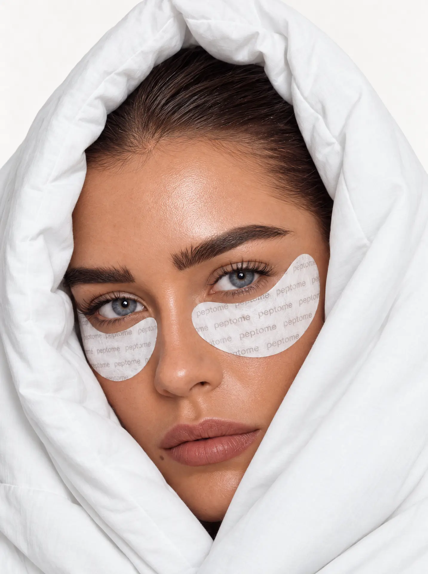 Model wearing Peptome copper peptide eye patches, wrapped in a white duvet