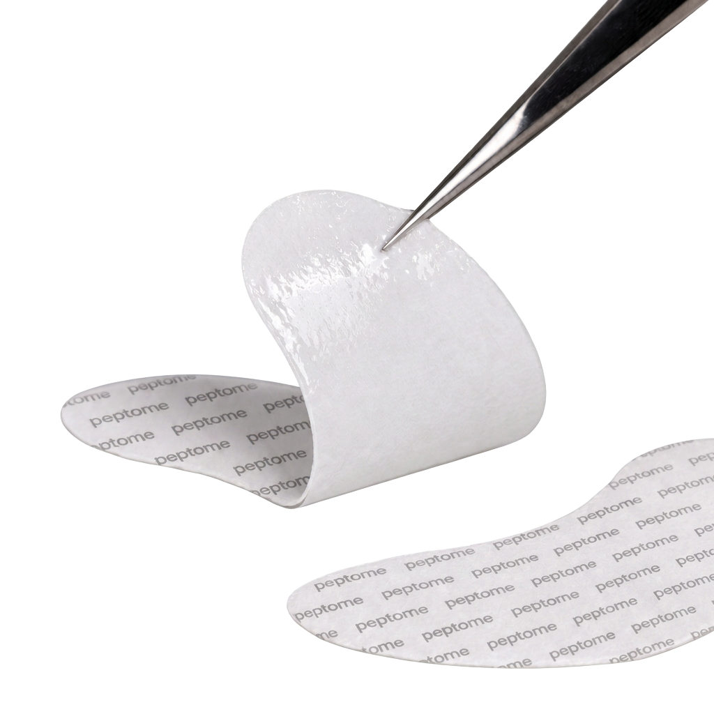 A Peptome hydrogel eye patch held on tweezers, printed with the peptome wordmark
