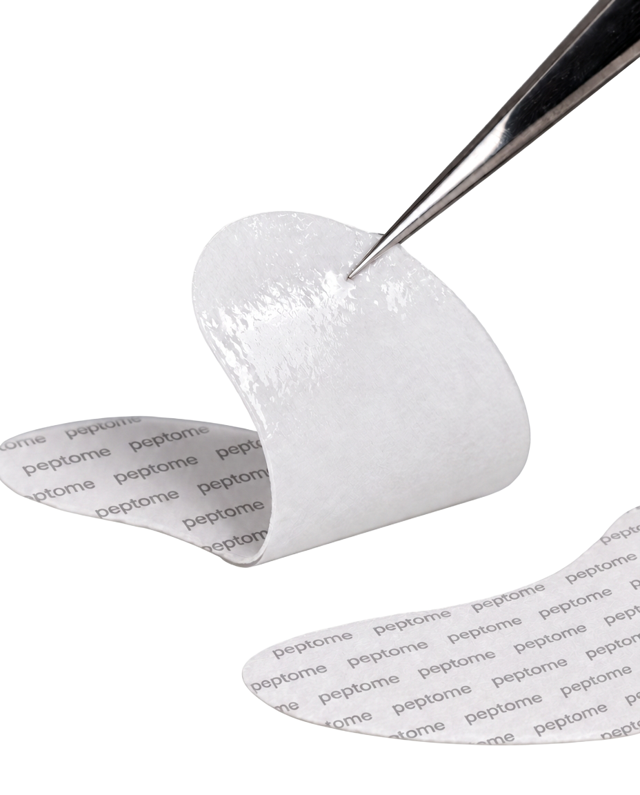 A Peptome hydrogel eye patch held on tweezers, printed with the peptome wordmark